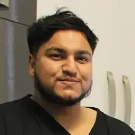 Young man with dark hair smiling in black scrubs