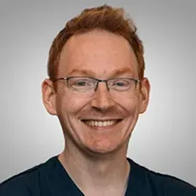 Smiling red-haired man wearing glasses and scrubs