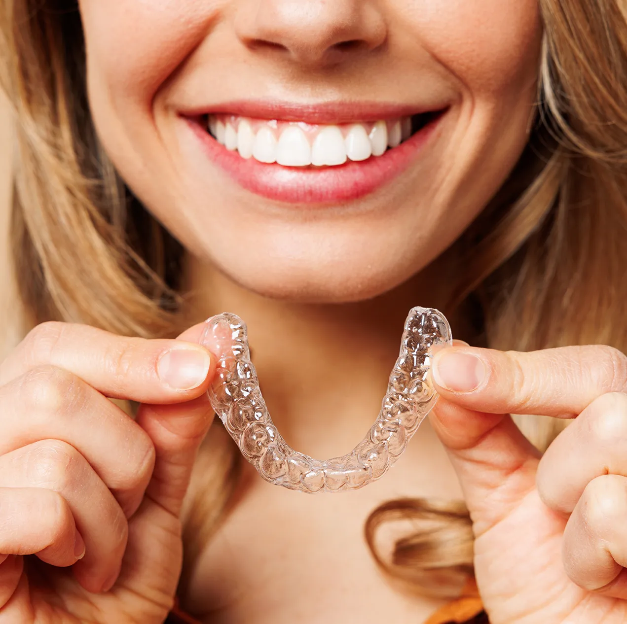 Smiling woman holding a clear dental aligner tray