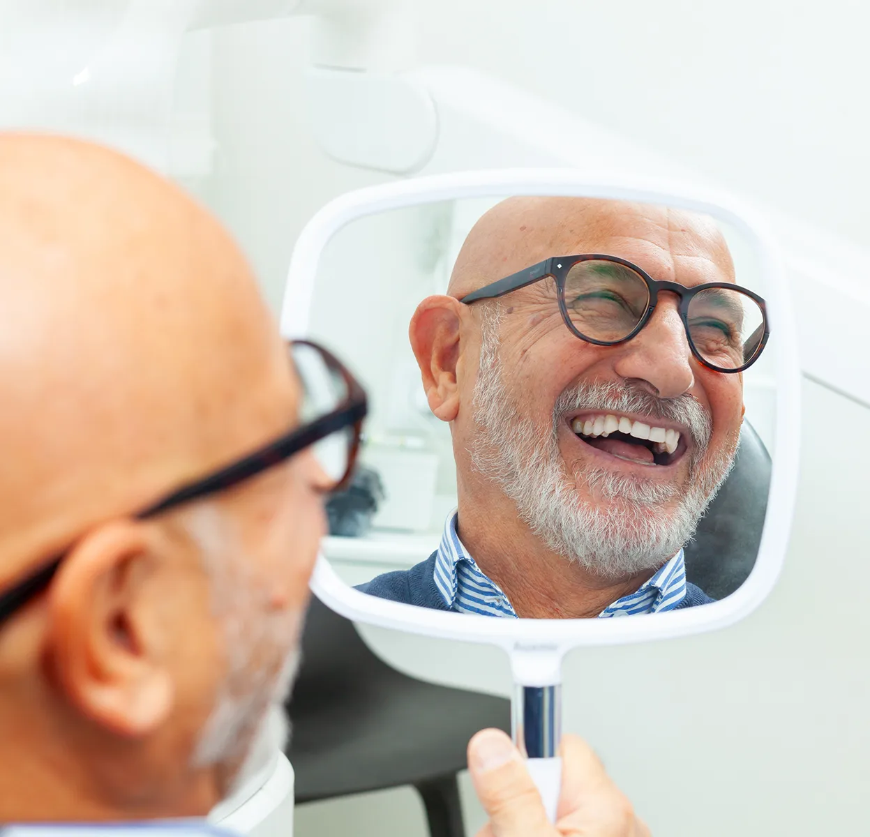 Elderly man smiling at his reflection in handheld mirror